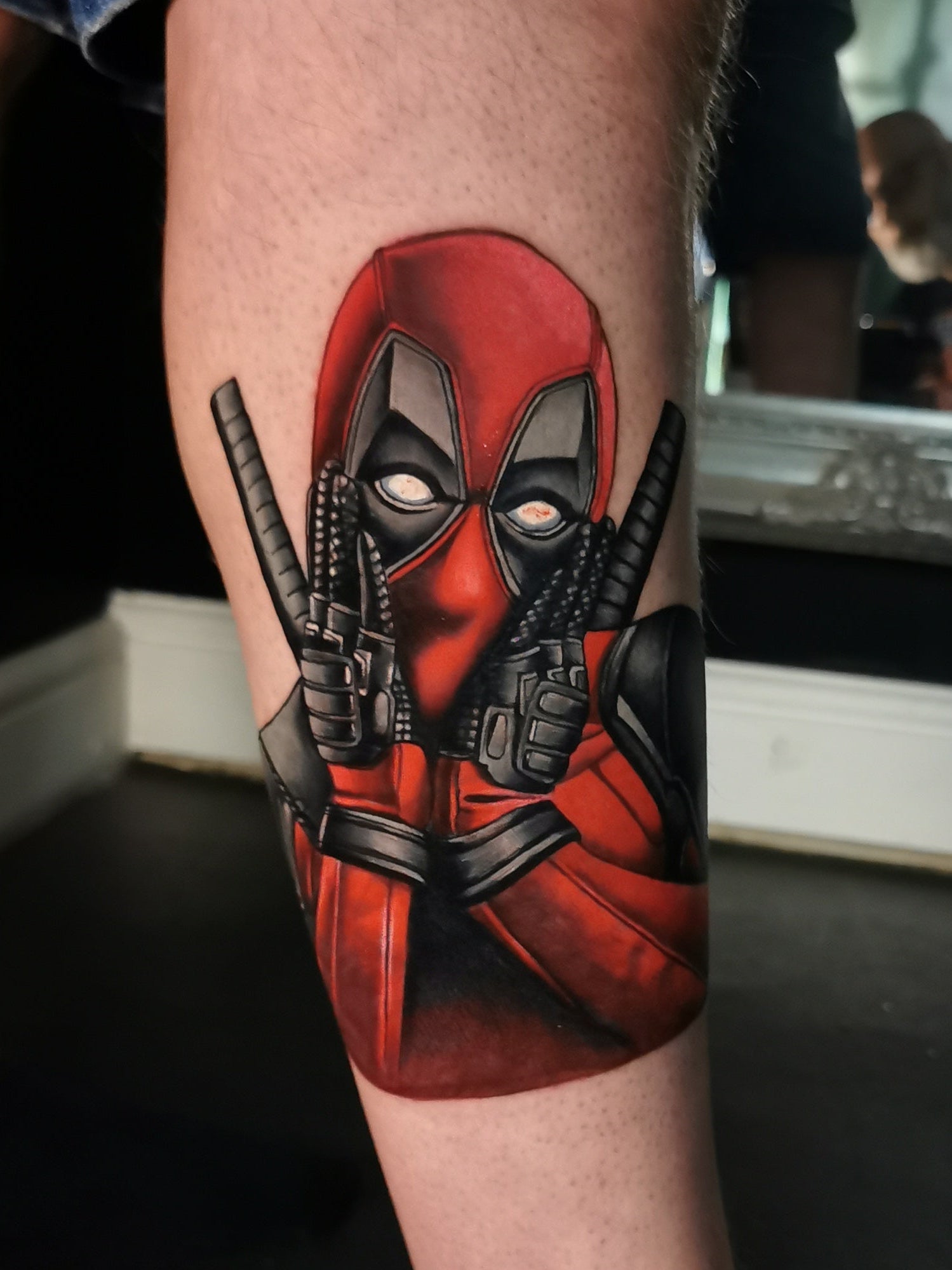 Deadpool tattoo on a person's leg with a mirror reflection in the background